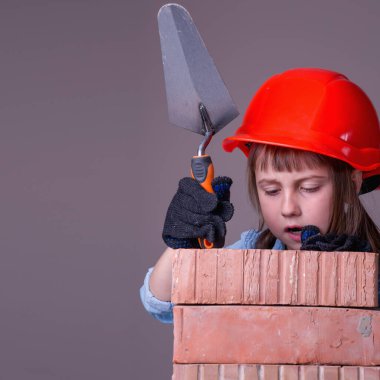 Şirin küçük kız müteahhidin komik görüntüsü tuğla duvar örüyor. İnşaat ve onarım hizmetleri kavramı.