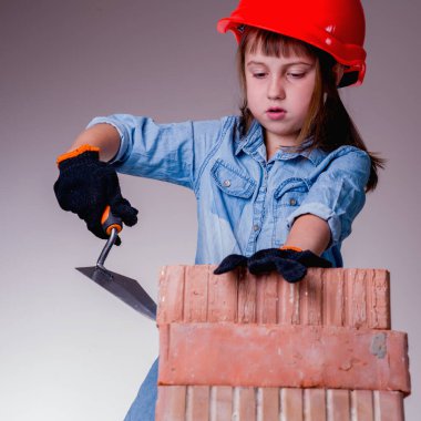 Şirin küçük kız müteahhidin esprili görüntüsü tuğla ev inşa ediyor. İnşaat ve onarım hizmetleri kavramı.