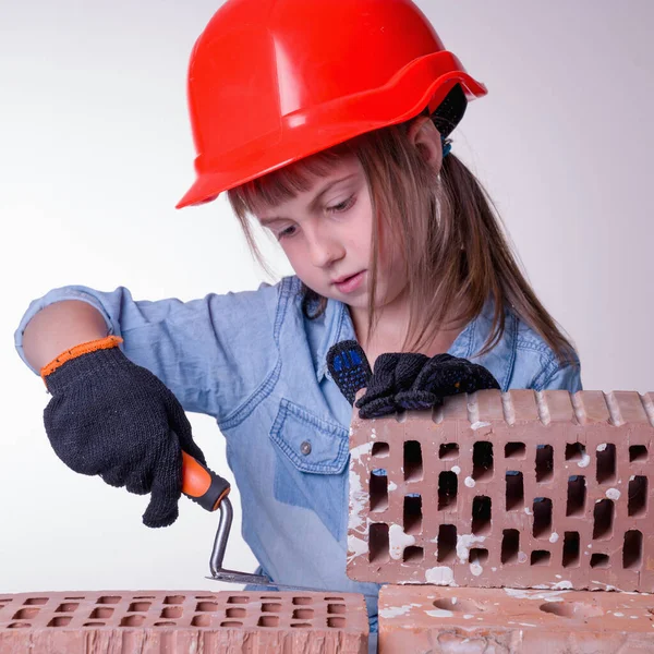 Best home builder. Humorous image of cute little child girl builder builds a brick wall. Building and repair services concept.