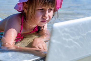 Her zaman ve her yerde öğrenmek. Küçük tatlı kızın komik portresini kapat ve dışarıda tropikal denizde dizüstü bilgisayarla öğrenme..