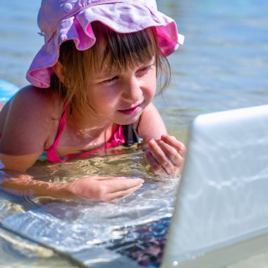 Küçük tatlı bir kızın komik portresi tropikal denizde dizüstü bilgisayarla uzaktan öğreniyor..