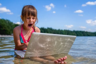 İşten dinlenmek ya da dinlenmek: tropikal denizde dizüstü bilgisayarla çalışan küçük tatlı bir kızın komik portresi.