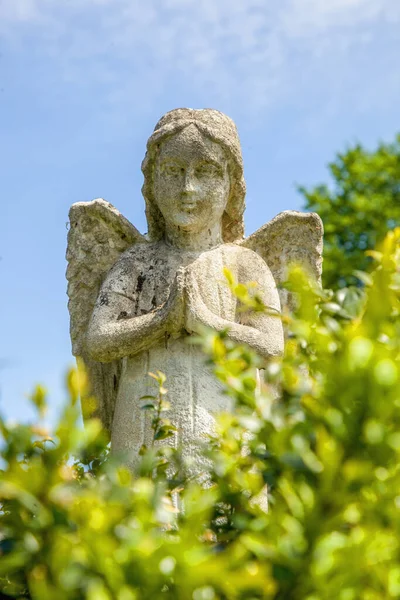 Praying angel. Ancient stone statue on a blue sky. Vertical image. Ancient statue.