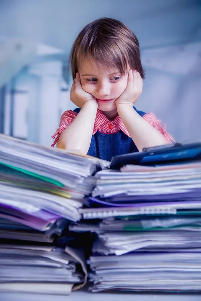 Tired and exhausted  business child girl working alone in office with a lot of documents. Humorous portrait. Selective focus on eyes.