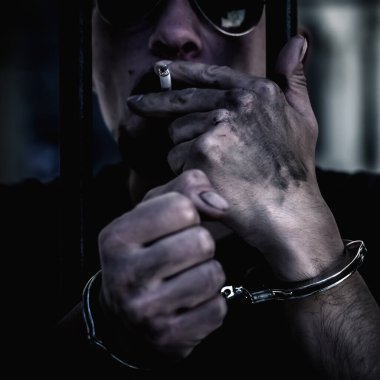 Tutuklu ve kelepçeli bir adamın, parmaklıklar arkasından sigara içtiği için hapsedilmiş portresini yakından çek. Gangster konsepti. 