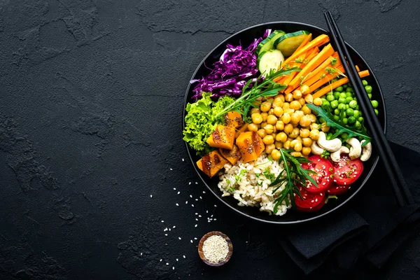 Bowl dish with brown rice, cucumber, tomato, green peas, red cabbage, chickpea, fresh lettuce salad and cashew nuts. Healthy balanced eating