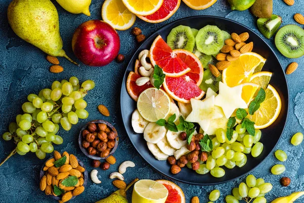 Healthy vegetarian bowl dish with fresh fruits and nuts. Plate with raw apple, orange, grapefruit, banana, kiwi, lemon, grape, almond, hazelnut and cashew nuts. Healthy balanced eating