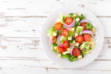Domates, marul, soğan ve peynir Beyaz ahşap zemin üzerinde taze sebze salatası. Sağlıklı vejetaryen yemek. Üstten görünüm