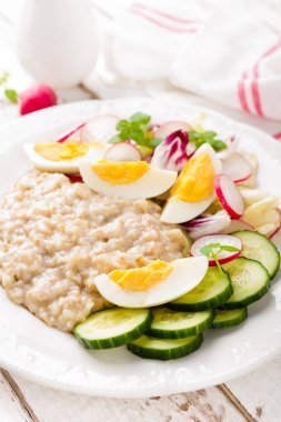 Haşlanmış yumurta ve taze turp, salatalık ve marul sebze salatası ile yulaf lapası. Sağlıklı diyet kahvaltı