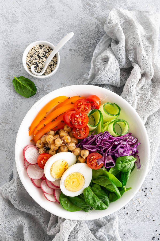 Buddha bowl salad with chickpeas, sweet pepper, tomato, cucumber, red cabbage kale, fresh radish, spinach leaves and boiled egg, healthy eating concept, top view, flat lay