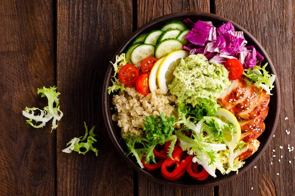 Buddha bowl dish. Healthy balanced lunch with quinoa, grilled chicken meat, lettuce salad, pepper, cucumber, tomato and avocado guacamole with lemon