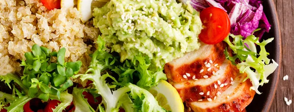 Buddha bowl dish. Healthy balanced lunch with quinoa, grilled chicken meat, lettuce salad, pepper, cucumber, tomato and avocado guacamole with lemon. Banner
