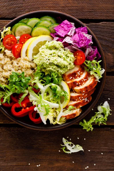 Buddha bowl dish. Healthy balanced lunch with quinoa, grilled chicken meat, lettuce salad, pepper, cucumber, tomato and avocado guacamole with lemon