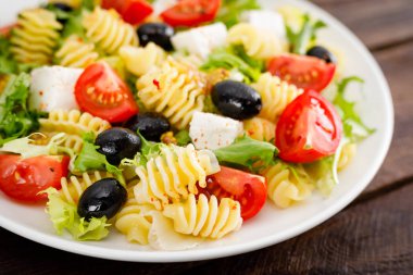İtalyan Makarna Salata taze domates, peynir, marul ve zeytin ahşap arka plan üzerinde. Akdeniz mutfağı. Öğle yemeği yemek. Sağlıklı bir diyet yemek