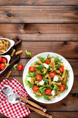 İtalyan makarna salatası kepekli düdük, taze domates, peynir, marul ve brokoli ahşap rustik arka plan üzerinde. Akdeniz mutfağı. Öğle yemeği yemek. Sağlıklı bir diyet yemek. Üstten görünüm
