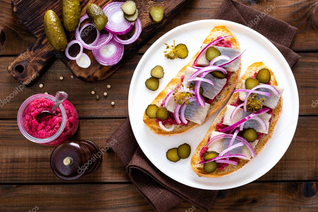 Delicious grilled sandwiches with herring, onion and beetroot sauce with horseradish on dark wooden rustic background. Danish cuisine. Top view