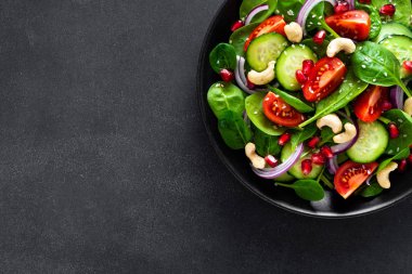 Taze salatalık, domates, soğan, nar, susam ve siyah arka plan üzerine kaju fıstığı ile ıspanak salatası. Sağlıklı vegan gıda. Üstten Görünüm