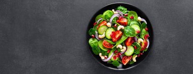 Taze salatalık, domates, soğan, nar, susam ve siyah arka plan üzerine kaju fıstığı ile ıspanak salatası. Sağlıklı vegan gıda. Üstten Görünüm. Afiş