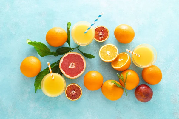 Orange and grapefruit freshly squeezed juice in glass and fresh fruits on a blue vivid background, top view