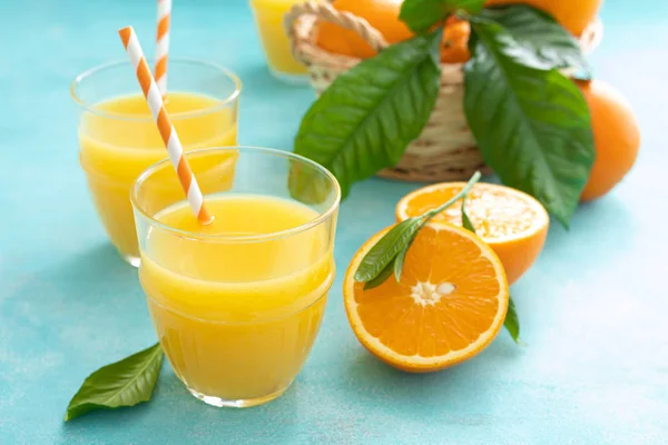 Orange freshly squeezed juice in glass and fresh fruits on a blue vivid background