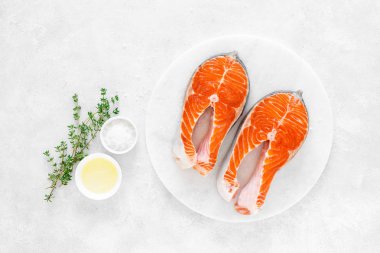 Beyaz tahta üzerinde yemek pişirmek için malzemelerle taze somon biftek, yukarıdan görünümü