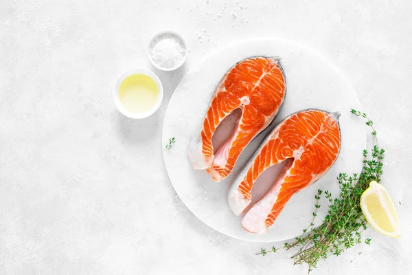 Beyaz tahta üzerinde yemek pişirmek için malzemelerle taze somon biftek, yukarıdan görünümü