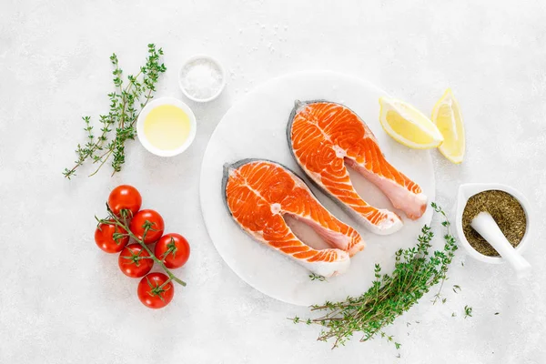Beyaz tahta üzerinde yemek pişirmek için malzemelerle taze somon biftek, yukarıdan görünümü
