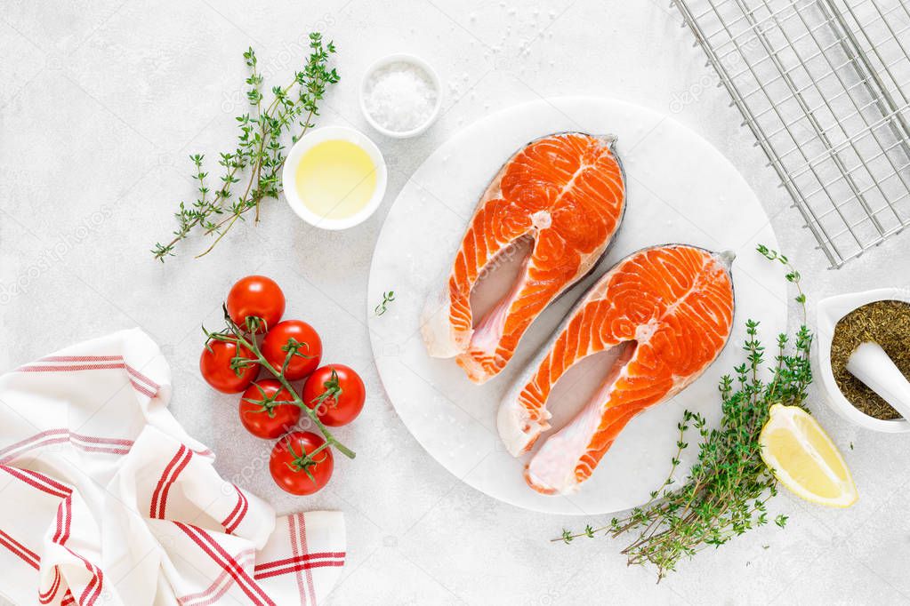 Fresh salmon steaks with ingredients for cooking on white board, view from above