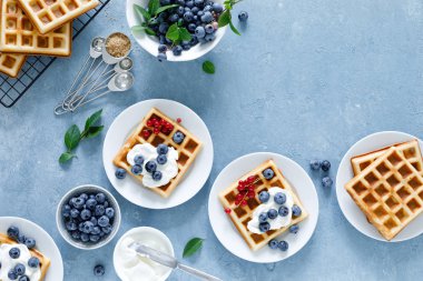 Mavi arka planda krem peyniri ve taze yaban mersini ile geleneksel Belçikalı Waffle, üst görünüm
