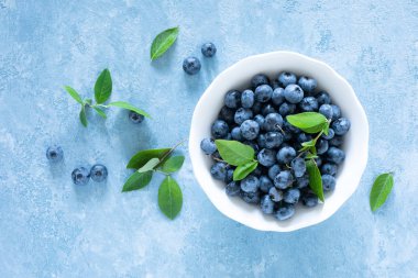 Mavi arka planda beyaz kase yaprakları ile yaban mersini, üst görünüm