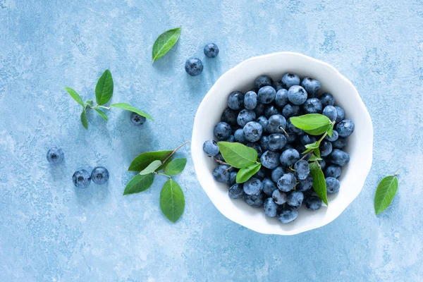 Mavi arka planda beyaz kase yaprakları ile yaban mersini, üst görünüm