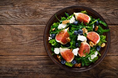 Ahşap arka planda keçi peyniri, yaban mersini, ceviz ve arugula ile incir salatası. Sağlıklı yiyecekler. Üstte görüntü