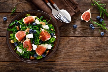 Ahşap arka planda keçi peyniri, yaban mersini, ceviz ve arugula ile incir salatası. Sağlıklı yiyecekler. Üstte görüntü