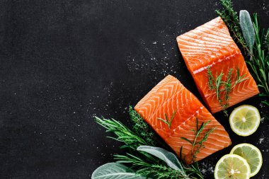 Somon. Pişirme maddeleri ile taze çiğ somon balık fileto, otlar ve siyah arka plan üzerinde limon, üst görünümü