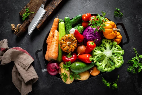 Culinary background with fresh raw vegetables on a black kitchen table, healthy vegetarian food concept, flat lay composition, top view