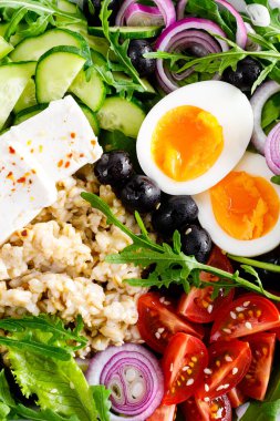 Yunan usulü sağlıklı kahvaltı kasesi yulaf lapası ve taze sebze salatası, marul, roka, zeytin, domates, salatalık, peynir ve haşlanmış yumurta.