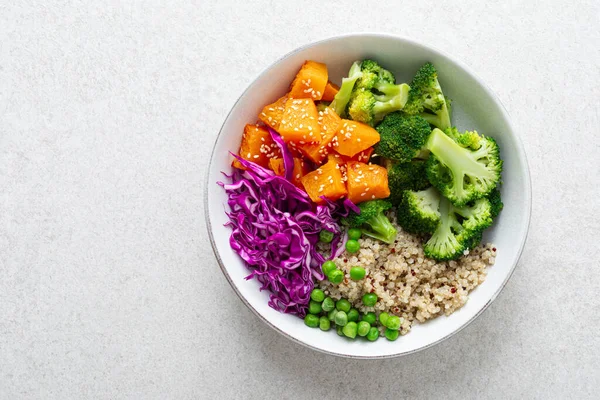 Vegetarian quinoa and broccoli lunch Buddha bowl with baked butternut squash or pumpkin, green peas and red cabbage, top down view