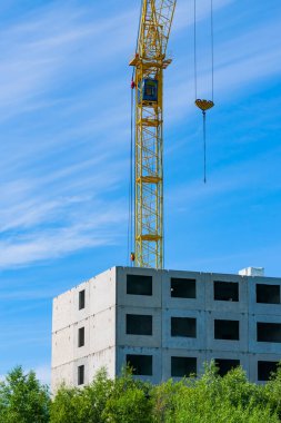 Mavi gökyüzüne karşı inşaat halindeki bir evin üzerinde bir vinç.