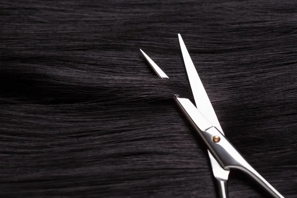 Eine Locke aus schwarzem Haar ist mit einer Schere getrimmt. — Stockfoto