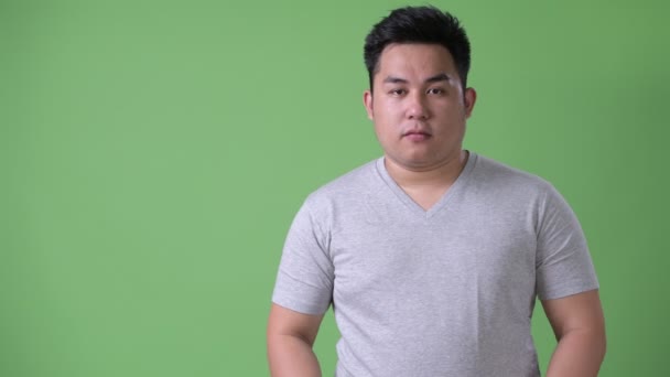 Młody przystojny nadwaga azjatycki człowiek na zielonym tle — Wideo stockowe