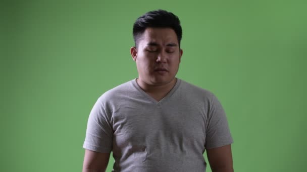 Νεαρό όμορφος υπέρβαρο Ασιατική άνθρωπο ενάντια σε πράσινο φόντο — Αρχείο Βίντεο