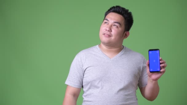 Młody przystojny nadwaga azjatycki człowiek na zielonym tle — Wideo stockowe