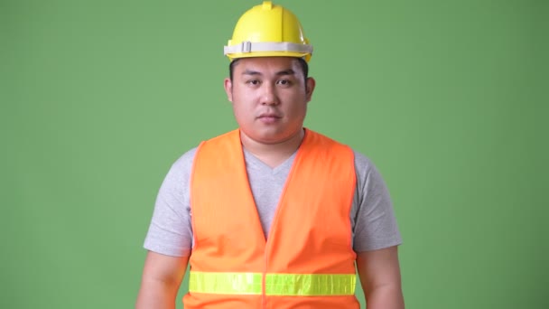 Όμορφος υπέρβαροι Ασίας νεαρός εργαζόμενος κατασκευή ενάντια σε πράσινο φόντο — Αρχείο Βίντεο