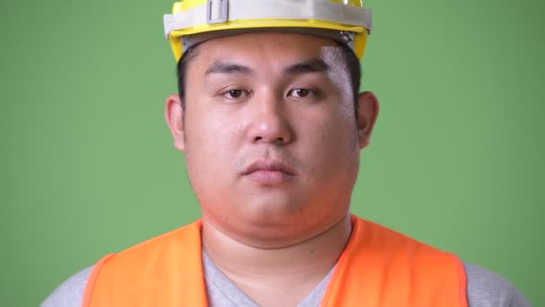 Jeune bel homme asiatique en surpoids travailleur de la construction sur fond vert — Video