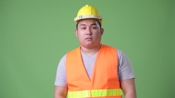Młody przystojny nadwagą Asian mężczyzna robotnik na zielonym tle — Wideo stockowe