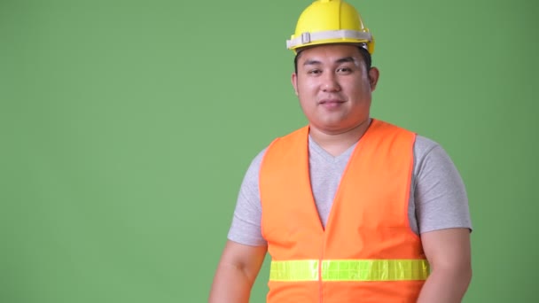 Молодой красивый толстый азиат строитель на зеленом фоне — стоковое видео