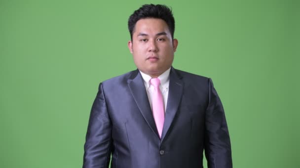 Молодой привлекательный толстый азиатский бизнесмен на зеленом фоне — стоковое видео
