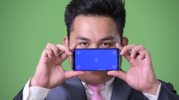 Ung, kjekk, overvektig asiatisk forretningsmann mot grønn bakgrunn – stockvideo
