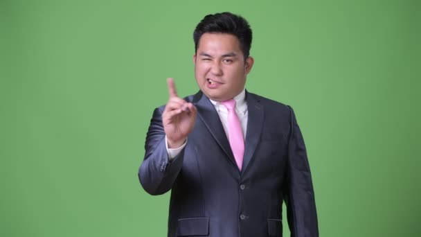 Jonge knappe overgewicht Aziatische zakenman tegen groene achtergrond — Stockvideo
