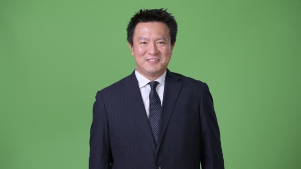 Mature Japanese businessman against green background — Stock Video